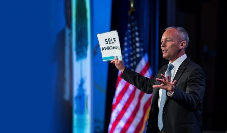 Speaker-in-suit-on-stage-holding-book-and-talking-to-audience
